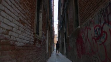 Adam duvarları tuğlayla kaplı dar bir sokakta yürür ve grafiti ile boyanır. Venedik, İtalya