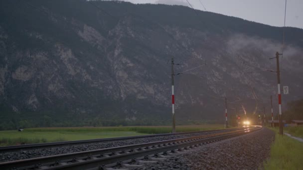 Поезд Освещенными Фарами Движется Железнодорожным Путям Сумерках Заднем Плане Видны — стоковое видео
