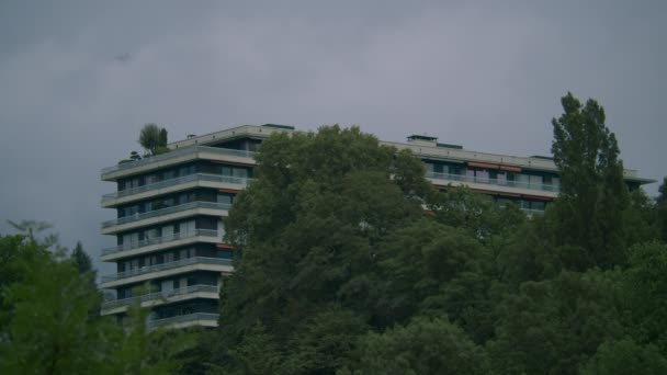 一座多层公寓楼 屋顶绿油油的 周围是密密麻麻的树梢和多云的天空 — 图库视频影像
