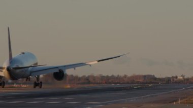 Uçak yavaş çekimde, dikey görüntüde, iniş takımları pist yüzeyinin hemen üstünde.