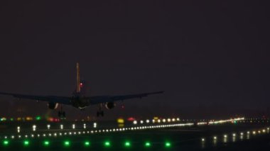 Uçak, gece ışıklarının ışıltısı altında bir piste iniyor.