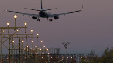 İniş takımlı uçak, alacakaranlıkta pist aydınlatma direklerinin önüne uzanıyor.