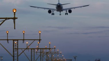 İniş takımlı uçak pist ışıkları üzerinde uçuyor, akşam gökyüzü arkaplanı