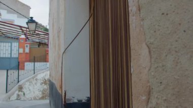 Kahverengi dikey kurdele perdelerinin yan görüntüsü eski bir evin yıpranmış beyaz duvarına karşı.