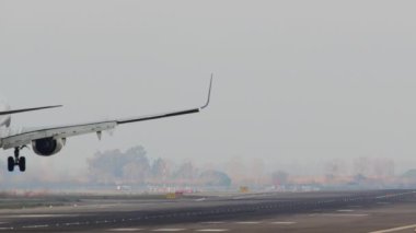 Uçak pistte iniş yaptıktan sonra duman çıkarıyor ve pist ışıkları görünüyor.