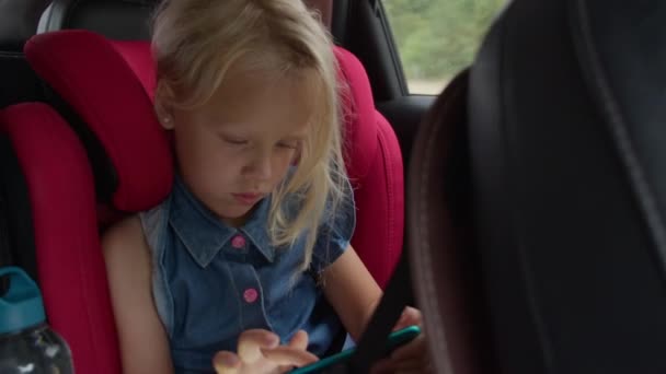 Młoda Dziewczyna Jest Pochłonięta Tabletką Podczas Siedzenia Jasnoczerwonym Foteliku Samochodowym — Wideo stockowe