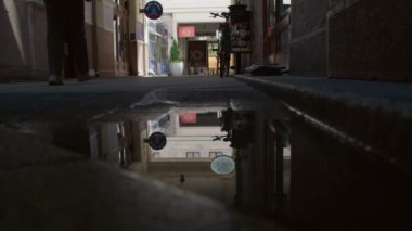 Budapeşte, Macaristan - 27 Haziran 2023: Bir yayanın siluetini ve sokakta bir bisikleti yakalayan bir su birikintisinde yansıma