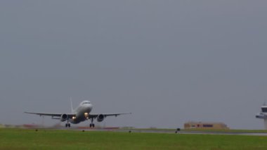 Bulutlu bir günde arka planda kontrol kulesi olan bir uçak pistten kalkıyor.
