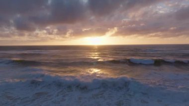 Güneş ışığının okyanus ve bulutlardan yansıdığı gün batımındaki dalgaların drone videosu