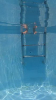 Mavi bir havuzda gözlük takan ve suyun altında yüzen genç bir kızın dikey videosu.