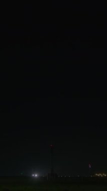 Gece kalkış yapan bir uçağı gösteren dikey video. Parlak ışıklarla aydınlatılmış ve karanlıkla çevrili.