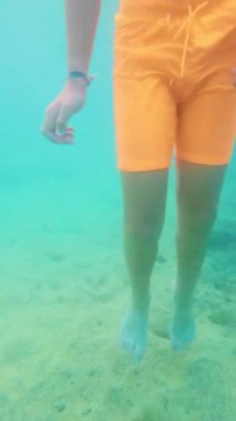 Yüzme gözlüğü takan, denizin altında yüzen bir çocuğun dikey videosu.