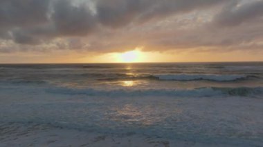Gün batımında okyanus dalgaları görünür güneş yansımaları ve bulut örtüsüyle