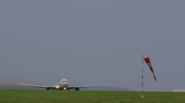 LISBON, PORTUGAL - 25 Nisan 2024: Parlak iniş ışıklarına sahip bir Delta Airlines uçağı, bulutlu bir arka planda görünür bir rüzgarlığa karşı kalkıyor