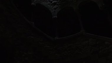 SINTRA, PORTUGAL - 25 Nisan 2024: Bir spiral taş kuyusunun içine yukarıya doğru bakan, yapraklı açıklıktan ışık filtreleri, yosun kaplı taşları vurguluyor