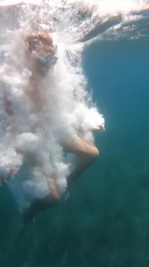 Yüzme gözlüğü takan ve havuzda yüzen bir gencin dikey videosu.