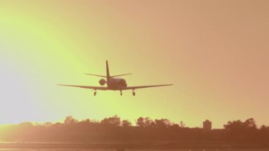 Gün batımında gökyüzüne iniş için küçük özel bir jet yaklaşıyor, pist ışıkları görünüyor.