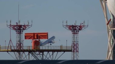 Uçak, havaalanının kırmızı ve beyaz radar kulelerinin arkasından kalkıyor.