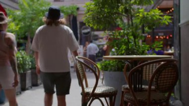 Budapeşte, Macaristan 'da Kiraly Caddesi' ndeki hasır sandalyeli kaldırım kafesi ön planda canlı yeşil bitkiler ve arka plandan geçen yayalar.