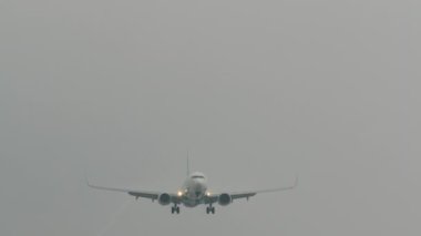 İniş takımları açık bir uçak sisli bir gökyüzünde iz bırakıyor, sanki yavaş çekimde çekilmiş gibi.