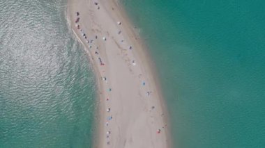 Possidi Cape, Halkidiki, Yunanistan 'ın doğrudan hava manzarası, insanlı, şemsiyeli, her iki tarafında da temiz turkuaz deniz bulunan dar bir plajı gösteriyor.