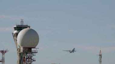 Radar kubbesi, arka planda bir uçağın havalandığı bir havaalanı kulesinde.