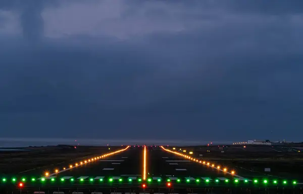 Pist gece yeşil ve sarı ışıklarla aydınlatılıyor. Arka planda okyanus manzarası var. Gökyüzü karanlık ve bulutlu.