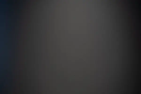 Düz koyu duvar yüzeyi, ince doku ve aydınlatma ile, minimalist bir arkaplan oluşturur.