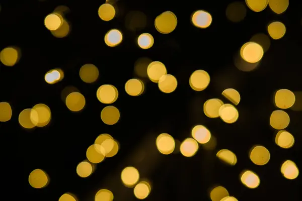 Karanlık bir zemin üzerinde parıldayan güzel altın bokeh ışıkları Noel ya da yeni yıl arifesi gibi şenlikler için mükemmel.