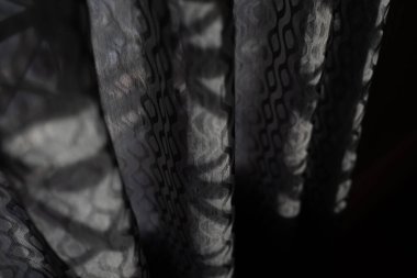 Geometrik tasarımlı gri bir perdedeki gölge deseni soyut bir görsel etki yaratıyor.