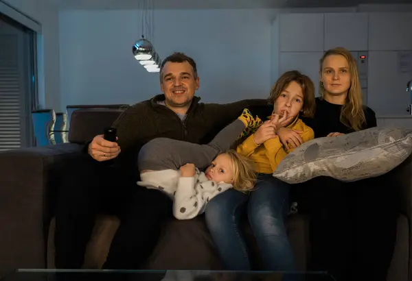 Oturma odasındaki kanepede oturan ve birlikte televizyon izleyen dört kişilik beyaz bir aile, rahat ve mutlu görünüyorlar.