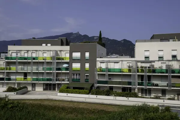 Yeşil ve beyaz balkonları ve arka planında bir dağ olan çağdaş bir apartman.