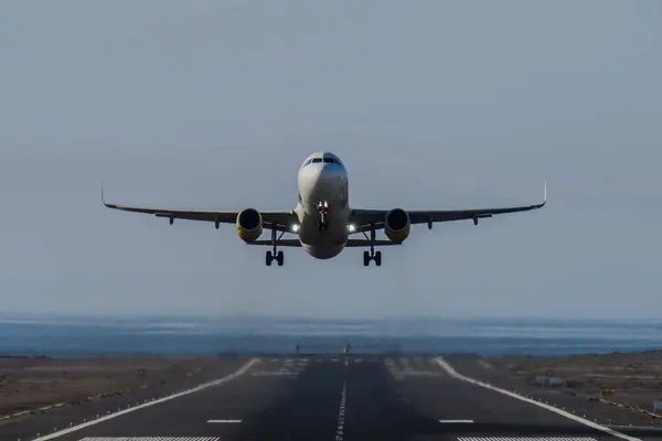 Arka planda açık gökyüzü ve okyanusla pistten kalkan bir uçağın ön görüntüsü.