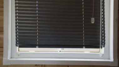 Siyah panjurların yakın çekimi beyaz pencere çerçevesinde kısmen açık. Panjurlar yatay çizgiler oluşturur ve küçük bir miktar ışığın geçmesine izin verir.