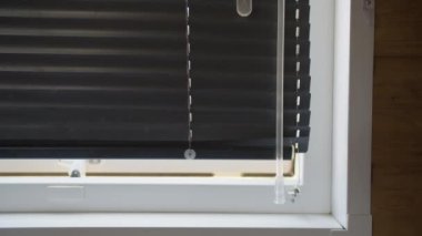 Beyaz bir pencere çerçevesindeki kısmen açık siyah panjurların detaylı görüntüsü, minimum ışığın filtrelenmesine olanak sağlıyor. Resim siyah panjurlar ve beyaz çerçeve arasındaki kontrastı vurgular.