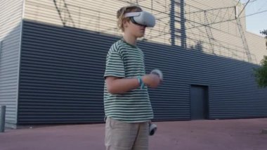 Sanal gerçeklik oyununa dalmış, VR kulaklık takmış, elinde joysticklerle bir alışveriş merkezinin duvarının yanında duruyor.