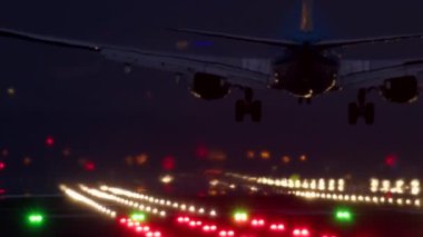 Uçak akşam saatlerinde piste inerken, silik şehir silueti ve şiddetli yağmur sırasında görülen pist ışıkları görülebiliyor.