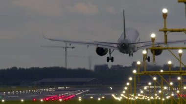 Airplane landing on a runway at dusk, showcasing the vibrant evening lights and serene sky