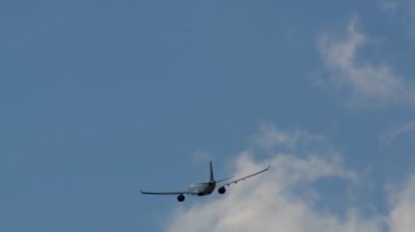 Alttan yakalanan bir uçak havalandıktan sonra yükseliyor, silueti ince bulutlu açık mavi bir gökyüzüne doğru yükseliyor.