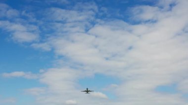 Parlak mavi gökyüzüne doğru havalanan bir uçağın alçak açılı görüntüsü dağınık bulutlarla uçağın altını çiziyor.