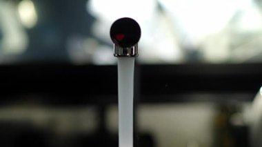 Işıl ışıl, şeffaf su, parlak krom musluktan akıyor. Mutfak arka planındaki bulanıklığa karşı saflıkla çağlıyor.