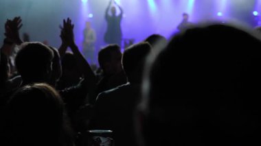 Seyircilerin canlı performansı, alkışlamaları ve heyecan içinde el kaldırmaları sahne ışıkları ve mor spot ışıklarıyla aydınlatılması, canlı bir atmosfer yaratıyor.