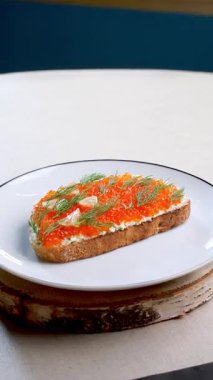 Lezzetli kırmızı havyar ve taze dereotla süslenmiş krem peynirli tost içeren gurme aperatifi koyu renk huş ağacının tepesinde duran saf beyaz tabağa güzelce yerleştirilmiş.