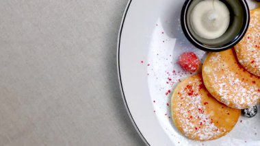 Pudra şekeri, ekşi krema ve böğürtlen reçeli ile küçük krepler beyaz bir tabakta dönüyor, bu da tatlı bir ziyafetin görsel olarak çekici bir sunumunu oluşturuyor