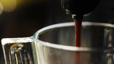 Profesyonel espresso makinesinden şeffaf cam bardağa dökülen taze demlenmiş kahve koyu sıvı yüzeyde büyüleyici dalgalanmalar yaratır.