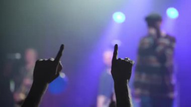 Rock 'n' roll hayranları canlı müzik performansı sırasında yoğun heyecan gösteriyorlar, ikonik şeytan boynuzlarıyla el kaldırıyorlar, ham enerjiyi ve konser atmosferinin tutkusunu somutlaştırıyorlar.