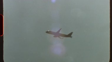 Süper 8 film Vintage tarzı ticari yolcu jeti bulutlu gökyüzünde süzülüyor, nostaljik film tahılları ve özgün ışık sızıntıları ile yakalanan analog sinematografiyi anımsatıyor.