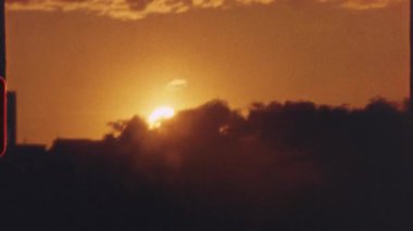 8 mm 'lik film - sıcak altın gün batımı kentsel ufuk çizgisini aydınlatan, alacakaranlık geçiş sırasında bulutlu gökyüzünde yayılan canlı turuncu renkler