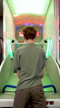 Atari basketbol makinesinin yanında duran genç oyuncu, yoğun bir şekilde odaklanarak parlak renkli oyun ortamında el ve göz koordinasyonuyla top atıyor.