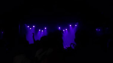Seyirciler canlı müzik deneyimine daldı, elleri havada ve mor ışıklar enerjik bir ortam yaratıyor.